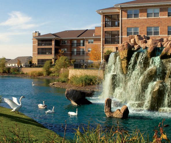 Apartment buildings beside a serene waterfall and swan pond.