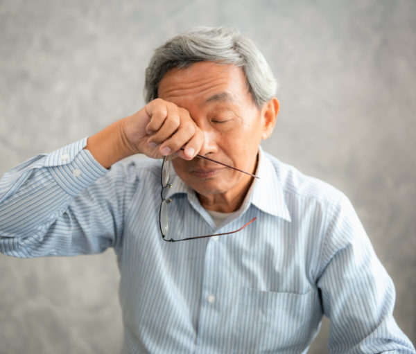 Senior man is holding eyeglasses and rubbing his tired eyes while reading e-book in tablet