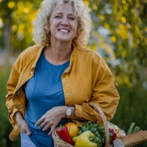 Portrait of mid adult housewife with curly hair standing on the street with hand in pocket, carrying shopping basket and looking at camera