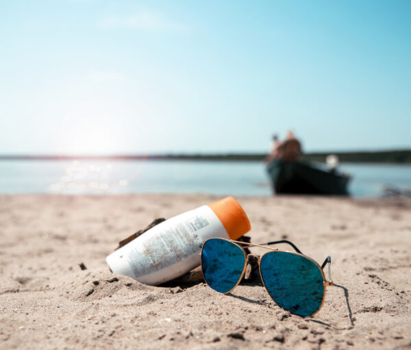 Sun lotion and sunglasses on the sea sand beach. Summer Holiday cream protection on sunny day. Copy space